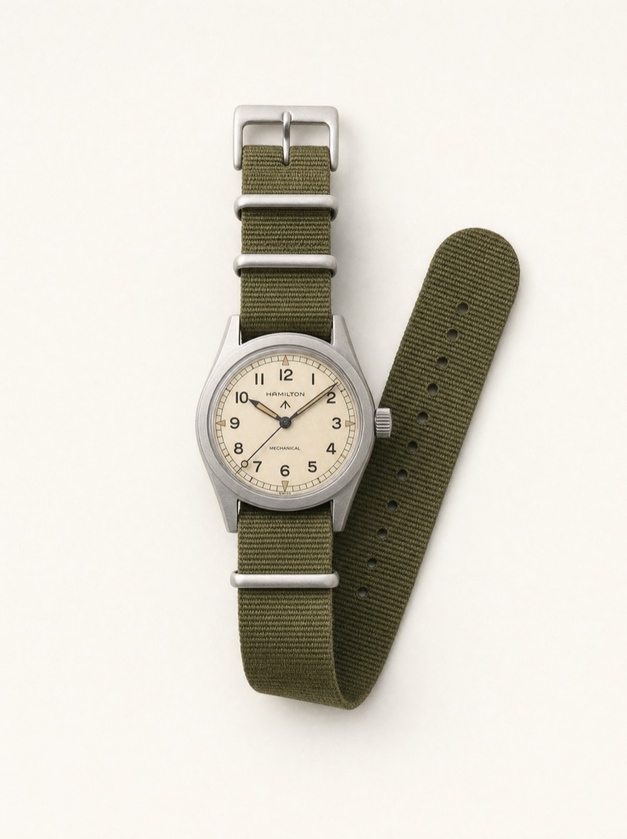 A field watch with an olive canvas strap, photographed on a bone-white seamless